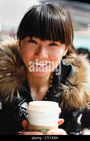 Giovane donna asiatica tenendo una tazza di caffè in un cafe' all'aperto e sorridente, Citta' di Xian, Cina Foto Stock