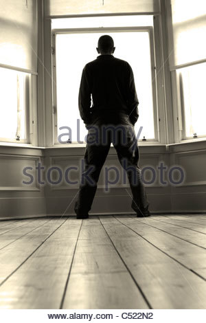 Uomo in silhouette a guardare fuori dalla finestra Foto Stock