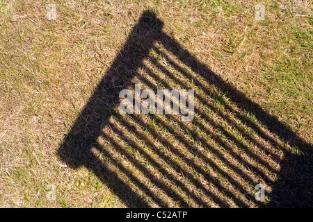 Ombra attraverso un secco e marrone giardino prato di legno sedia da giardino in estate il sole. Foto Stock