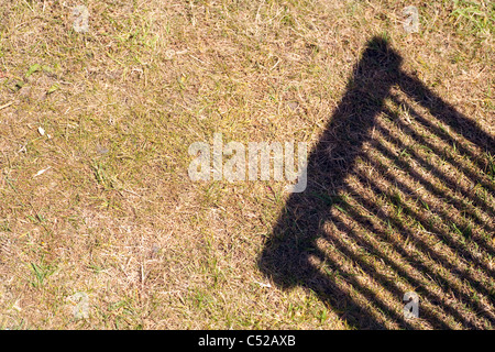 Ombra di una sedia da giardino contro un prato arido Foto Stock