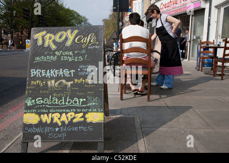 Persone che sono servite a Troia Cafe segno e tabelle su Shoreditch High Street, Londra Foto Stock