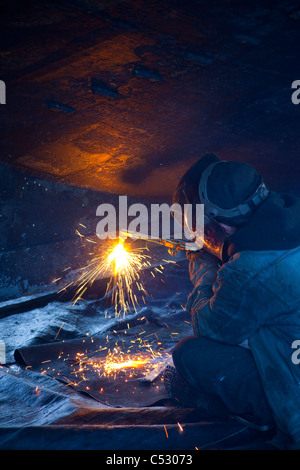 Operatore taglia raccordi di metallo fuori dello scafo di una barca, Kodiak cantiere, Saint Herman Harbour, Kodiak, vicino Isola, Alaska Foto Stock