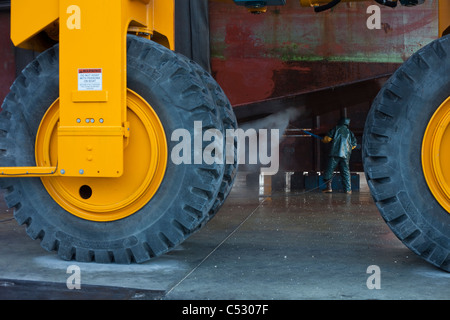 Guardando oltre i pneumatici di grandi dimensioni su un Marine Travelift, un membro di equipaggio lavaggi lo scafo, Kodiak Boat Yard, Alaska Foto Stock