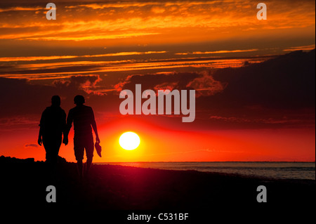 Giovane camminando mano nella mano lungo una spiaggia al tramonto, sulla costa di Norfolk, Inghilterra. Foto Stock
