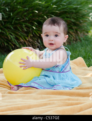 Un otto mesi baby caucasica bambina gioca con una sfera gialla all'esterno. Foto Stock