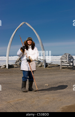 Inupiaq maschio eschimese hunter indossa il suo Eskimo parka , in piedi di fronte a un Bowhead whale osso arch e Umiaqs, Barrow, Alaska Foto Stock