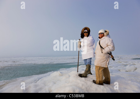 Inupiaq eschimese cacciatori in eskimo trasportare un fucile e bastone mentre guardano il mare Chukchi, Barrow, Alaska Foto Stock