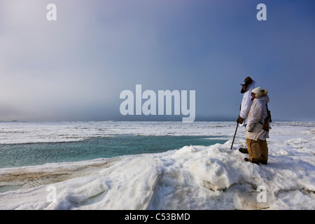 Inupiaq eschimese cacciatori in eskimo trasportare un fucile e bastone mentre guardano il mare Chukchi, Barrow, Alaska Foto Stock