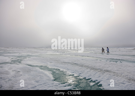 Inupiaq eschimese cacciatori trasportare un fucile e bastone mentre si cammina su Riva ghiaccio lungo il mare Chukchi, Barrow, Alaska Foto Stock