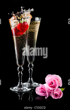 Due bicchieri di spumante di schizzi di vino (champagne) con rose di rosa e fragola su nero Foto Stock