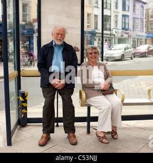 Un sorridenti coppia senior in attesa di autobus seduti in un bus shelter, REGNO UNITO Foto Stock