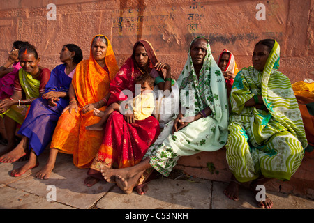 Gruppo di donne indiane in colorati saris sedute su gradini lungo le rive del fiume Gange Foto Stock