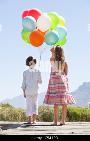 Vista posteriore dei fratelli giocando con palloncini a un molo Foto Stock