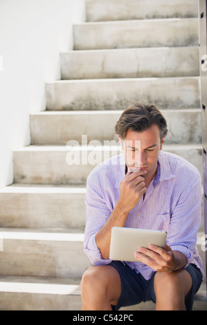Metà uomo adulto seduto sui gradini e utilizzando una tavoletta digitale Foto Stock