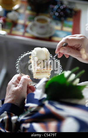 Femmina Senior mani tenendo una torta e prendendo un pezzo Foto Stock