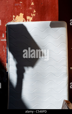 Ombra di un lampione sul materasso abbandonati per strada Foto Stock