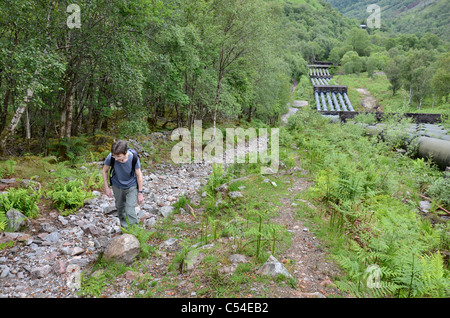 Un viandante sul sentiero accanto al gasdotto che corre da Blackwater serbatoio fino a Kinlochleven in Lochaber, Scotland, Regno Unito. Foto Stock