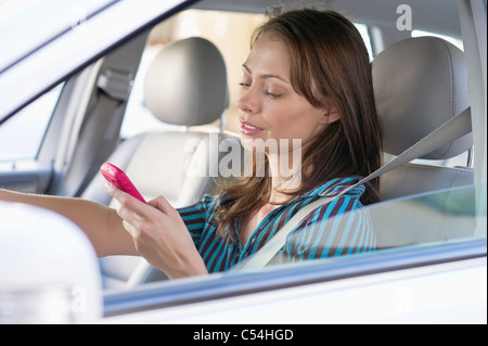 Bella giovane donna utilizzando un telefono cellulare mentre si è alla guida di un veicolo Foto Stock