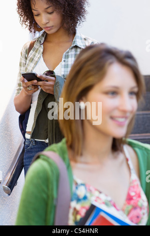 Close-up di una studentessa universitaria con African American donna utilizzando il telefono cellulare in background Foto Stock