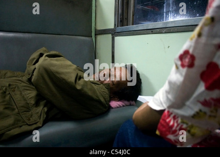 Un uomo stanco è dormire su un sedile di Chiang Mai legato treno passeggeri nel nord della Thailandia. Foto Stock