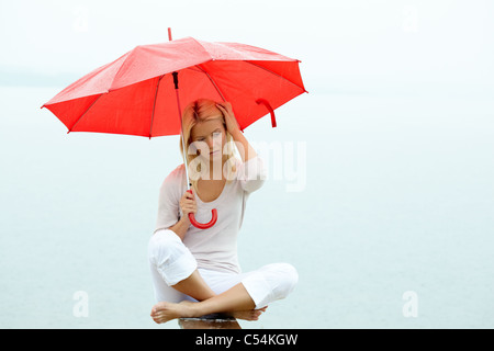 Ritratto di giovane triste donna seduta con ombrello sotto la pioggia Foto Stock