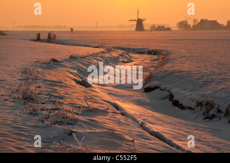 I Paesi Bassi, Lollum, Windmill e congelate in flusso di neve al tramonto. Foto Stock