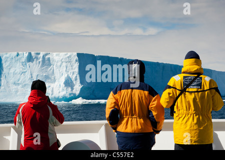 Primo piano 3 Antarctic expedition cruise passeggeri sulle navi esterno deck guarda come giganti blu iceberg galleggianti da in Antartide indossando giallo e rosso eskimo Foto Stock