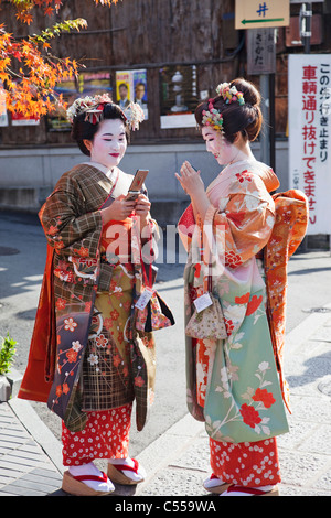 Due donne Geisha vestita in kimono utilizzando i telefoni cellulari, Higashiyama Ward, prefettura di Kyoto, Kinki Regione, Honshu, Giappone Foto Stock