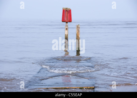 Avviso di colore rosso marcatore & dolce Sciabordare di onde su pontile in legno come marea avanza, Cleethorpes, South Humberside, REGNO UNITO Foto Stock