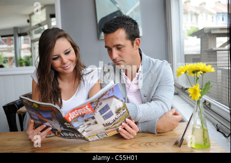 Coppia giovane cercando di acquistare o affittare una proprietà sfogliare ultime case albergo magazine a Brighton Regno Unito Foto Stock