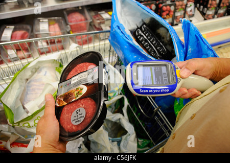 Acquirente di tecnologia per supermercati Tesco che utilizza la scansione portatile durante l'acquisto dispositivo di scansione codice a barre degli alimenti sul display digitale per il download & Paga fino al Regno Unito Foto Stock