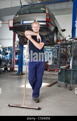 A piena lunghezza Ritratto di giovane uomo appoggiato sulla scopa in garage Foto Stock