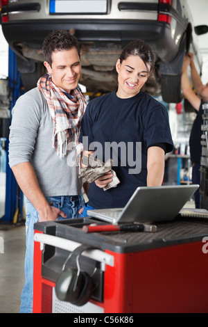 Lavoratore di sesso femminile che utilizza computer portatile mentre in piedi accanto al client in garage con persona in background Foto Stock