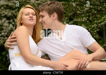 Amare giovane toccando e parlare mentre sdraiati su un banco in un parco con fiori Foto Stock