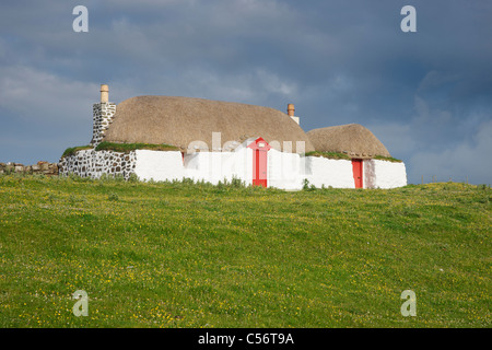 Un bianco, cottage con il tetto di paglia con porta rossa a Sraid Ruad, Tiree, Argyll, Scotland, Regno Unito. Foto Stock