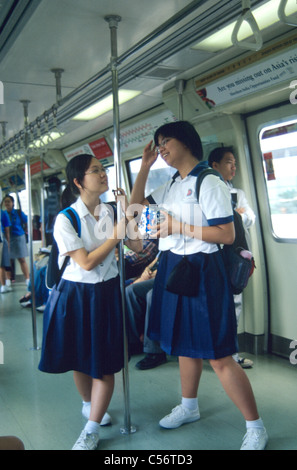 Due scuole di Singapore le ragazze in uniformi di parlare sulla massa locale MRT di transito Foto Stock