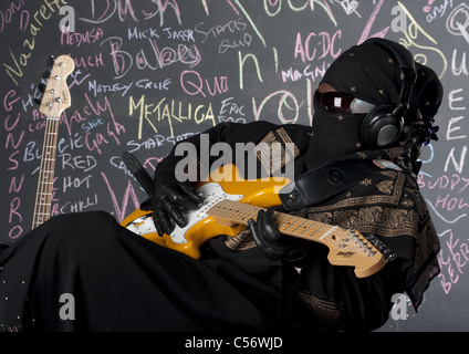 Vestito femminile in piena Purdah suonare chitarra solista in una fascia di metalli pesanti Foto Stock