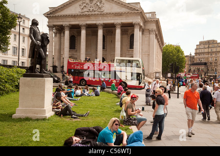 La Gente seduta sul prato di Trafalgar Square al di fuori della Galleria Nazionale, St Martin nei campi in background, Londra Foto Stock