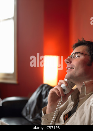 Uomo che parla al telefono nella stanza vivente Foto Stock