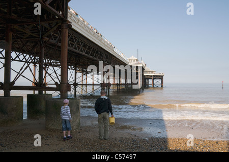 Un giovane ragazzo con un adulto, camminando verso la riva ad unirsi ad altri il tentativo di cattura di granchi sotto Cromer Pier. Foto Stock