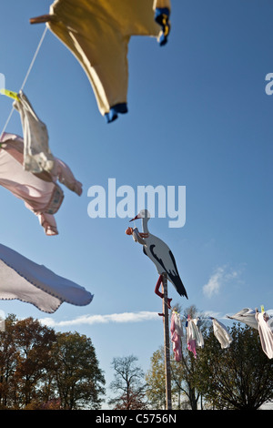 I Paesi Bassi, Lattrop, cicogna in legno con baby doll, per mostrare che un bambino è nato. Vestiti del bambino su stendibiancheria. Foto Stock