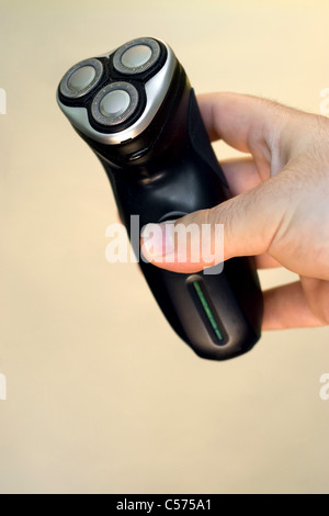 Una mano che tiene un rasoio elettrico isolato su un colore di sfondo a tinta unita. Profondità di campo. Foto Stock