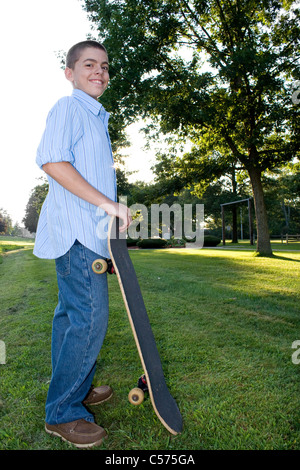 Un ragazzo nei suoi primi ragazzi felicemente in piedi con il suo skateboard. Foto Stock