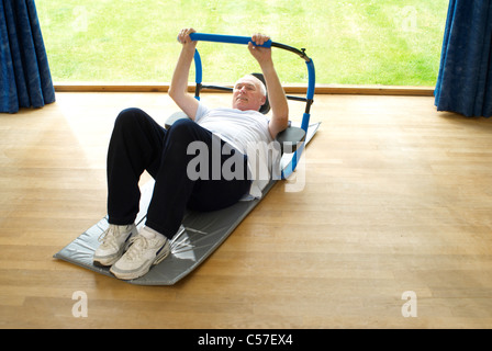 Uomo vecchio facendo sit ups in ambienti interni Foto Stock