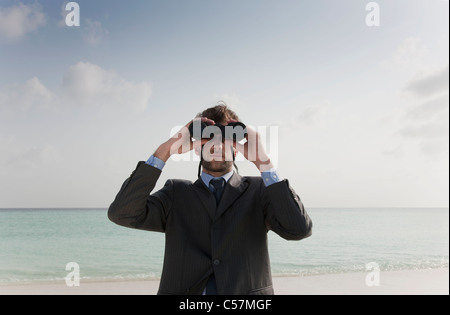 Imprenditore utilizzando il binocolo sulla spiaggia Foto Stock