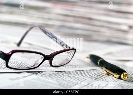 Gli occhiali da lettura e una penna a sfera giacciono su un giornale Foto Stock