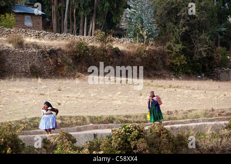 Due donna a piedi lungo i sentieri di Amantani, andare circa le loro attività quotidiane. Foto Stock