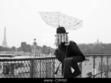 Una giovane donna Ride come il suo ombrello è rovesciato dal vento al di sopra del Place de la Concorde. Parigi. Francia Foto Stock