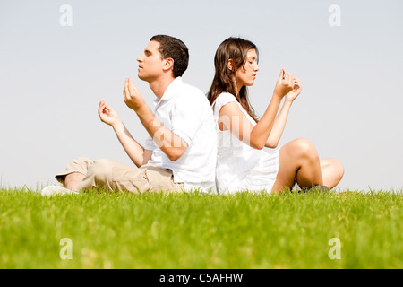 Coppia giovane seduto su erba e facendo la meditazione Foto Stock