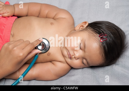 Sleeping Baby girl ottenendo un battito cardiaco esame con infermieri delicatamente la mano tenendo uno stetoscopio il battito del cuore del bambino durante la health check up Foto Stock